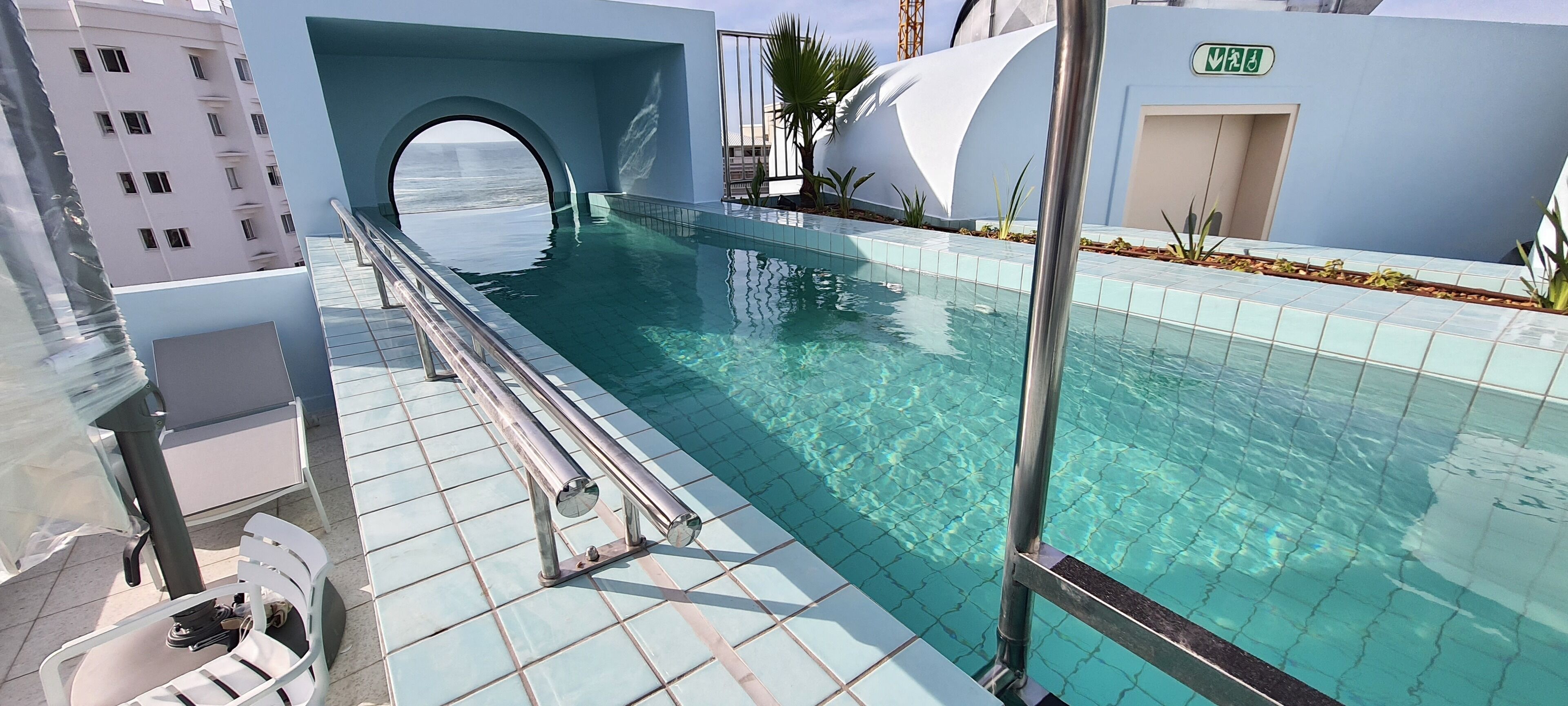 A modern pool area with clear water, a glass barrier, and a view of the ocean through an arched opening.
