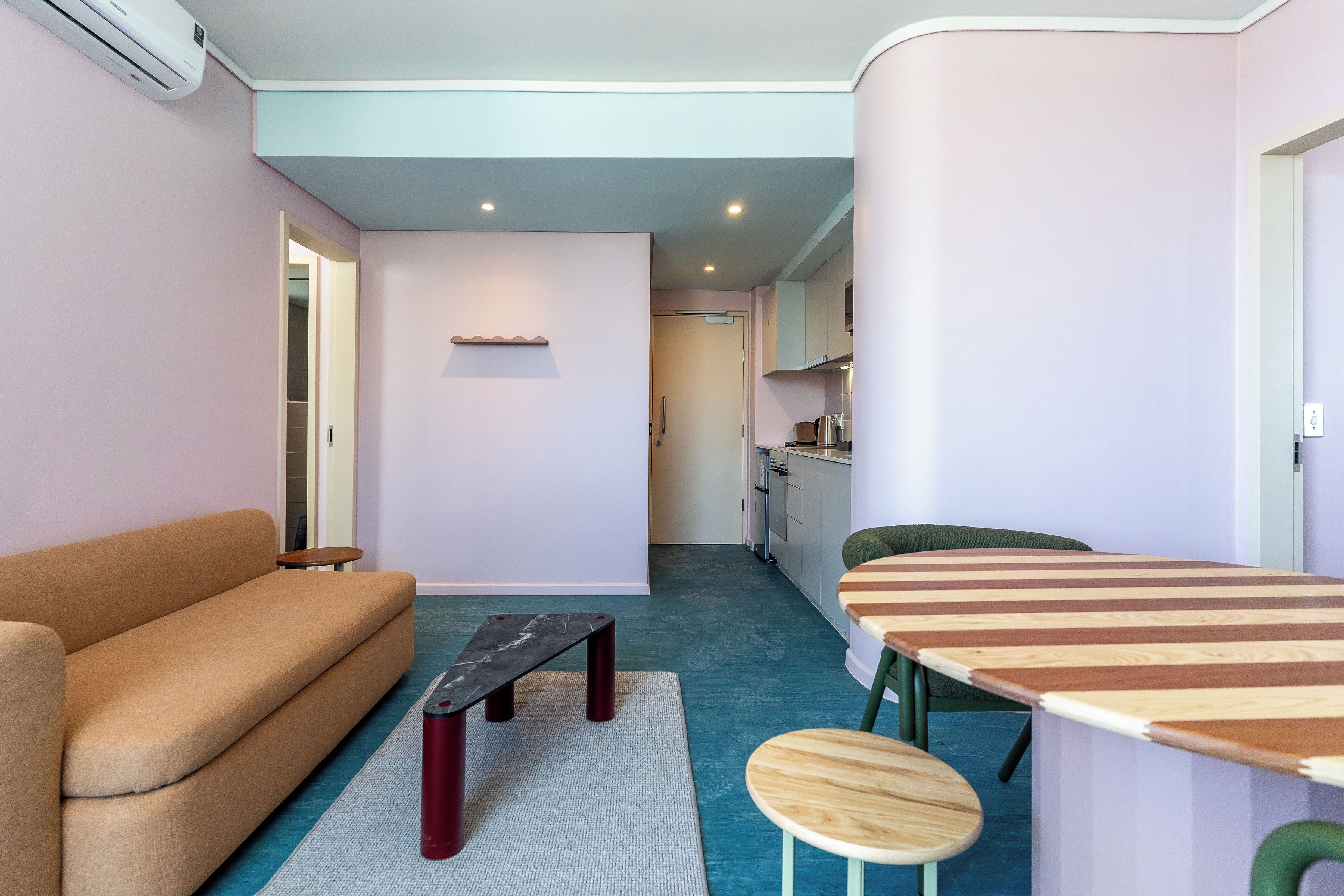 A compact living space with a sofa, a small table, a dining table with chairs, and a kitchen area in the background.