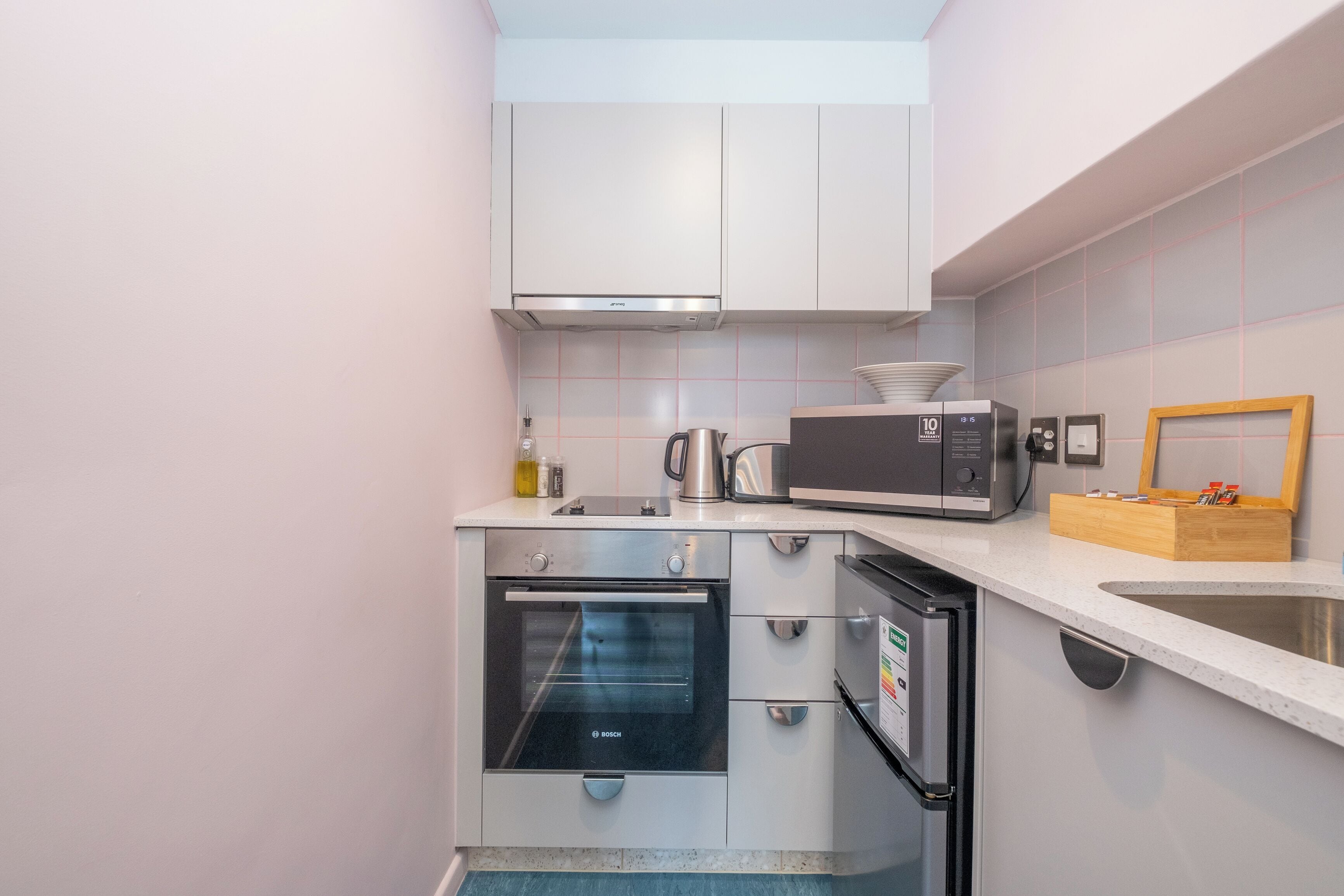 A compact kitchen with white cabinets, a Bosch oven, a microwave, and a sink.