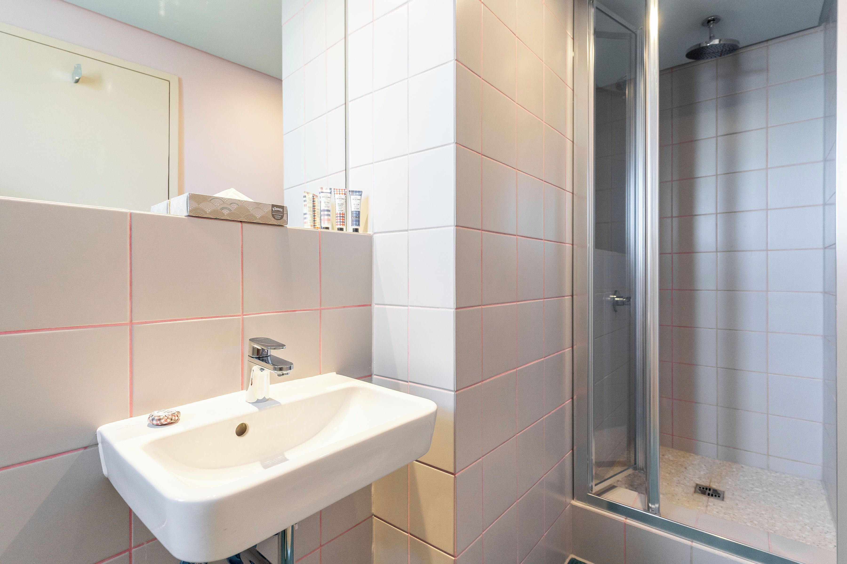 A bathroom with a sink, mirror, and shower.