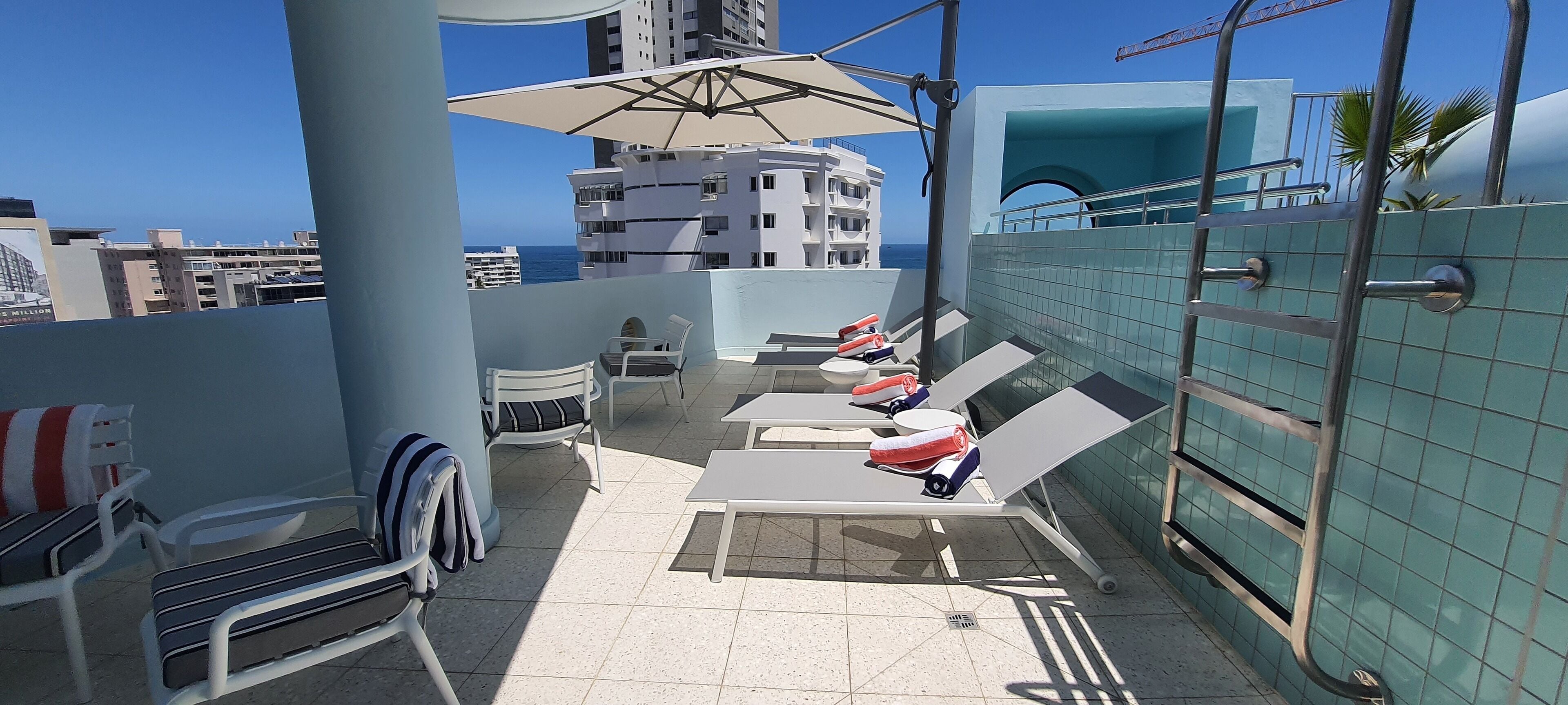 A rooftop terrace with sun loungers, a table, and an umbrella.