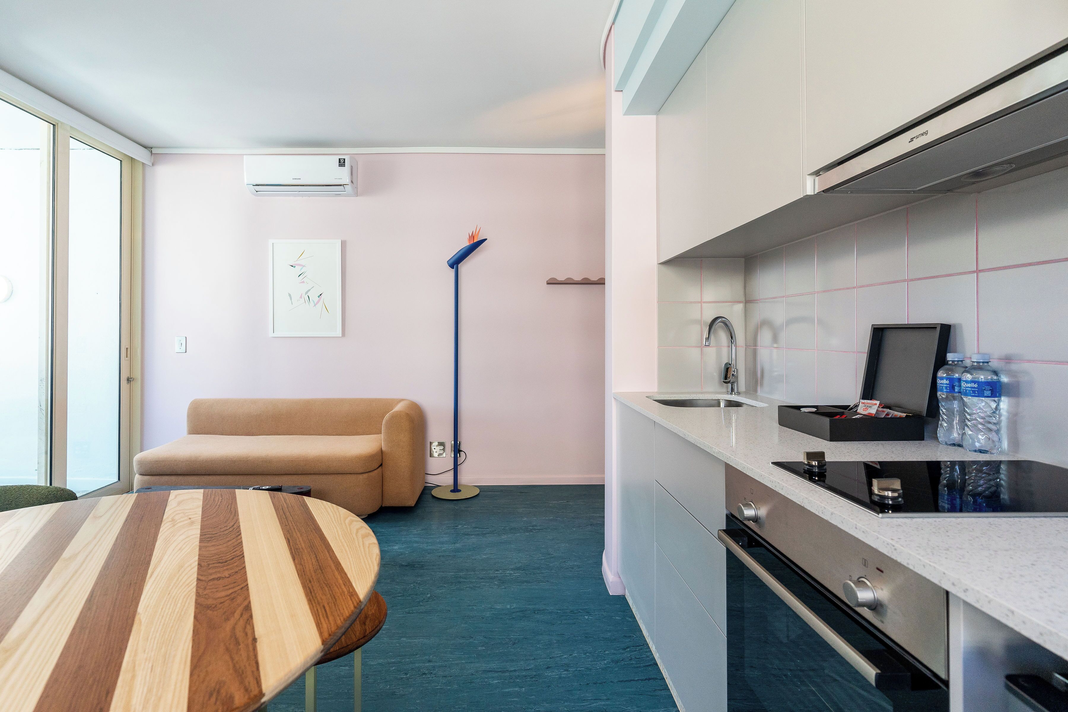 Une cuisine moderne dotée d’une cuisinière intégrée, d’un évier et de meubles blancs. Le salon comprend un canapé beige et une table ronde en bois.