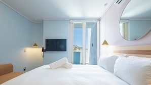 A hotel room with a large bed, a TV mounted on the wall, a phone, and a view of the outside.