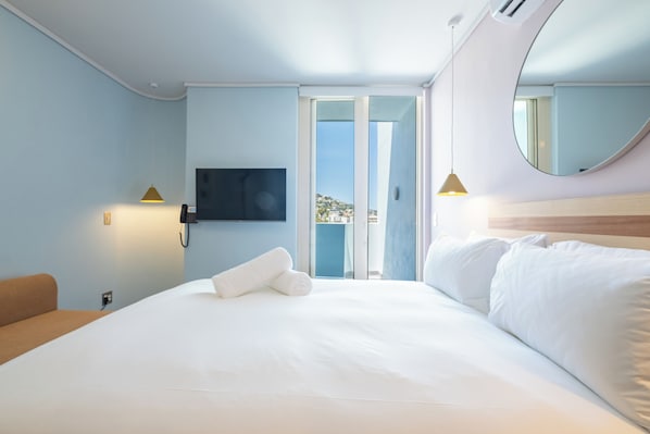 A hotel room with a large bed, a TV mounted on the wall, a phone, and a view of the outside. - The Tropicana Hotel (Cape Town)