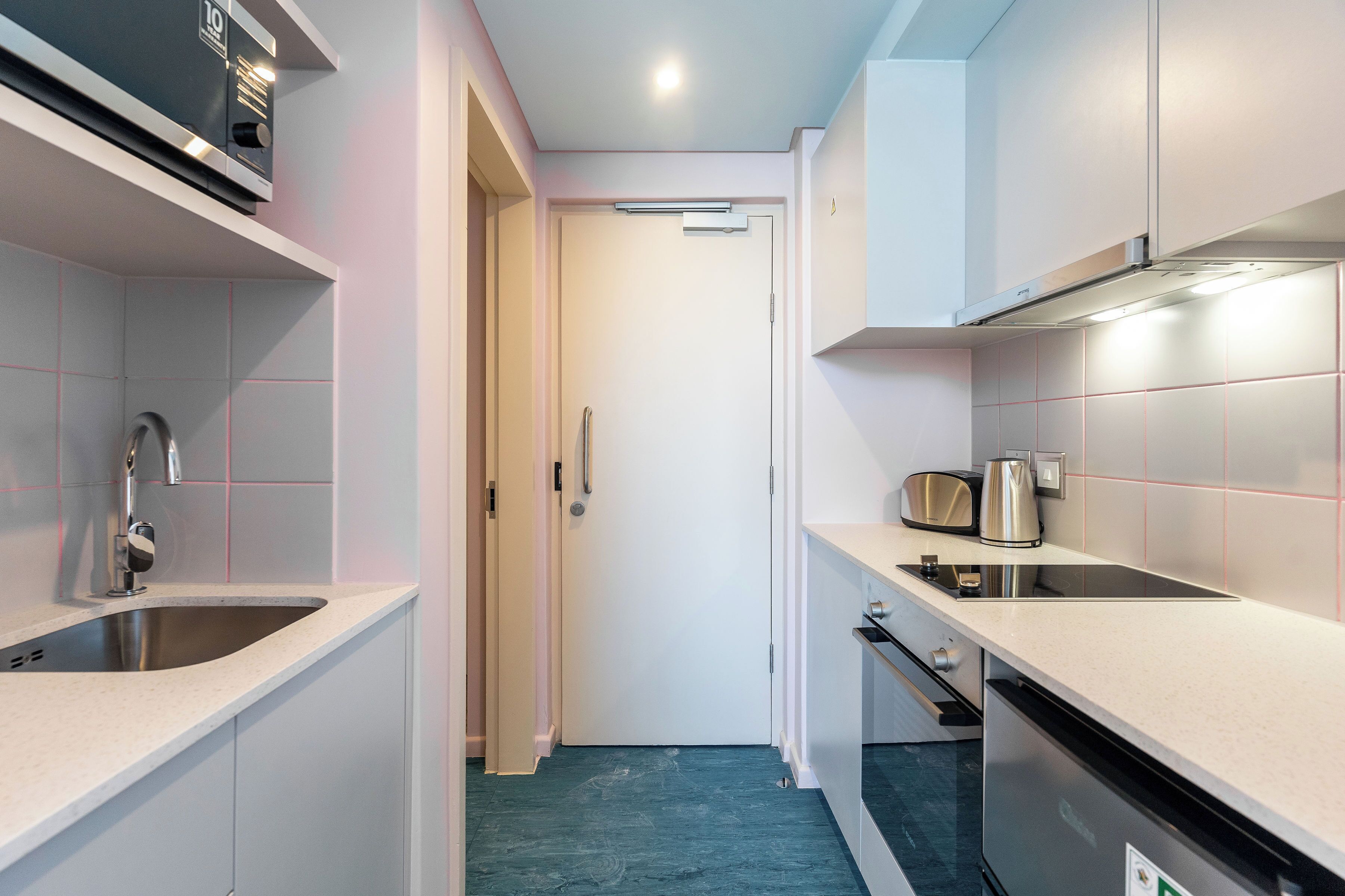 A modern kitchen with white cabinets, stainless steel appliances, and a teal floor.