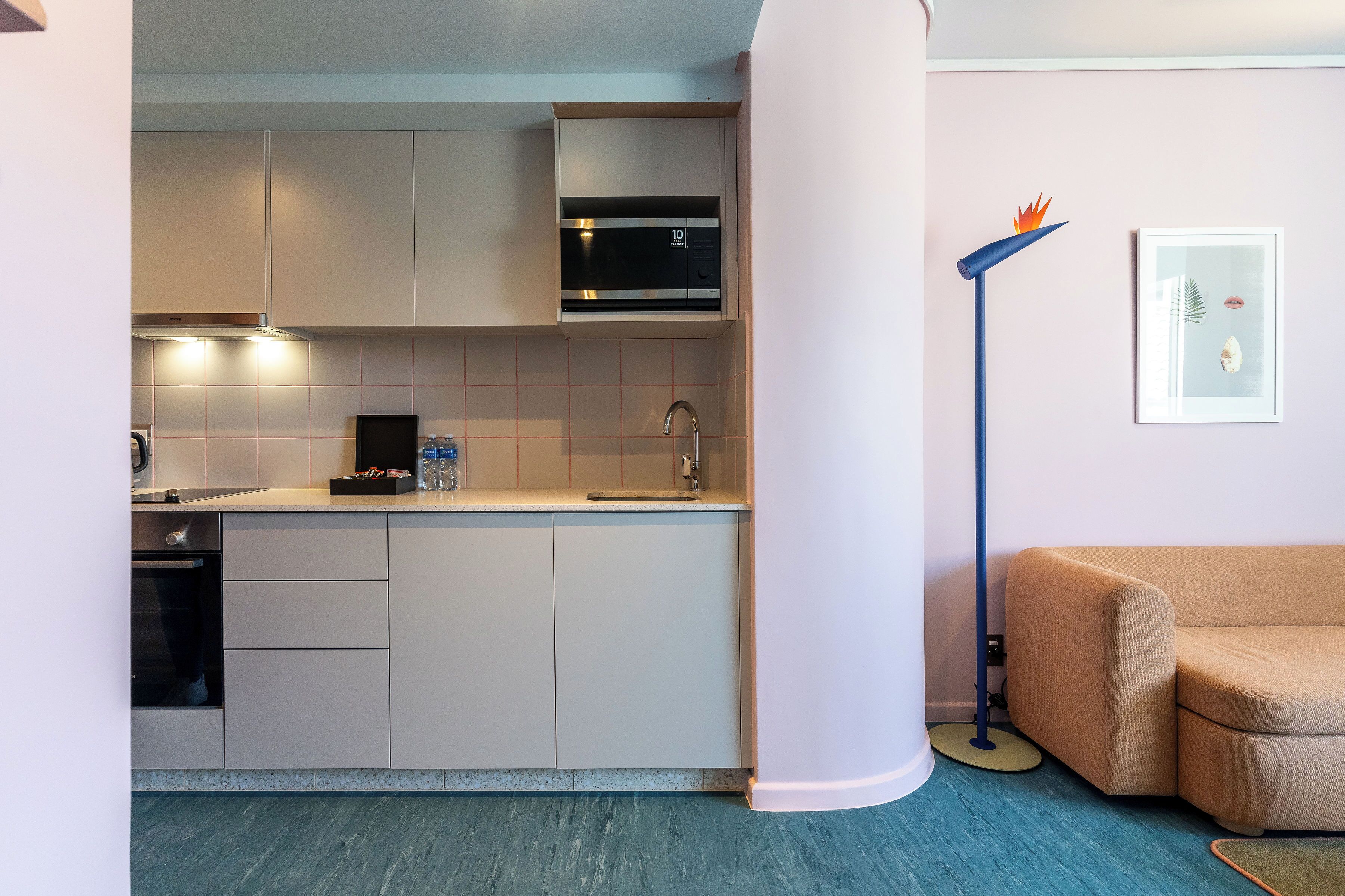 A modern kitchen with a built-in microwave, oven, and sink. There is a beige sofa in the adjacent living area.