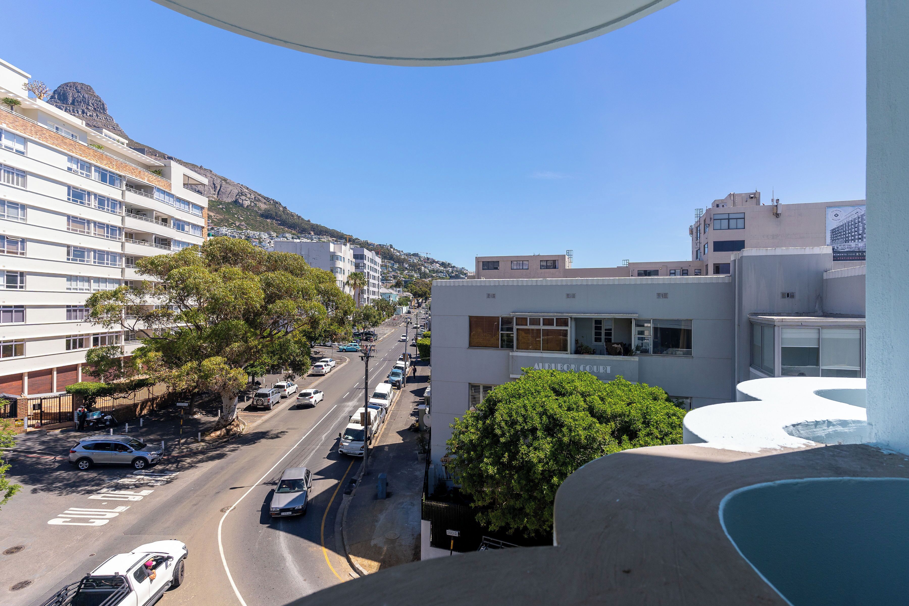 Vista de una calle con edificios, coches aparcados y cielo despejado.
