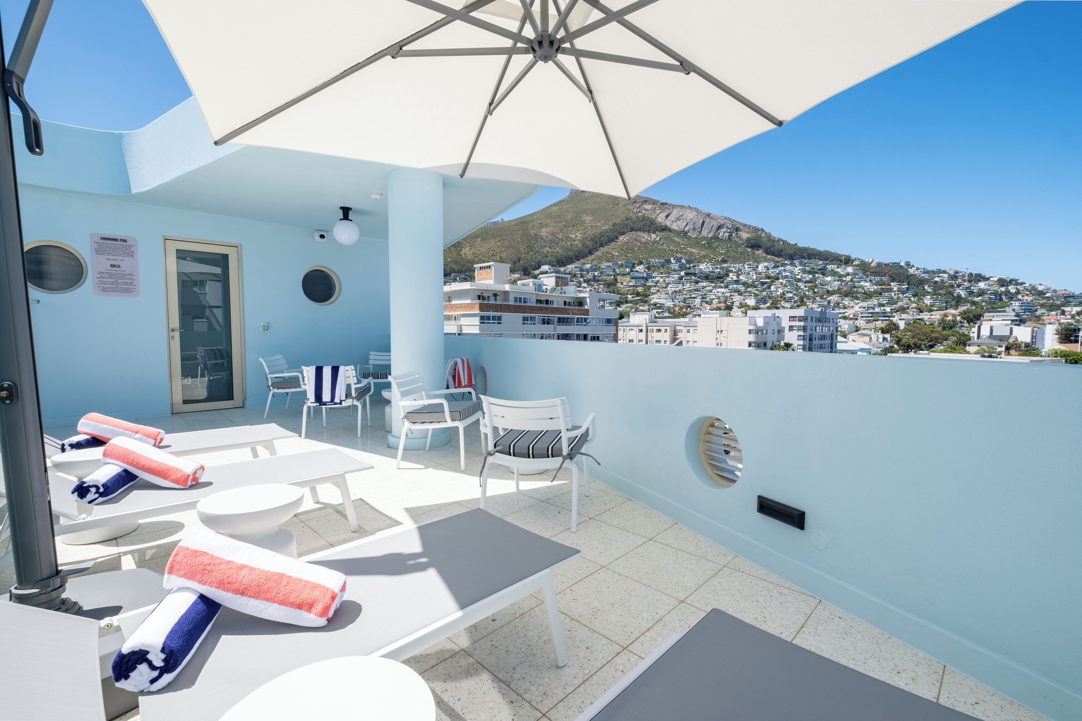 Une terrasse sur le toit, avec des chaises longues, une table et une vue sur une ville située sur une colline.