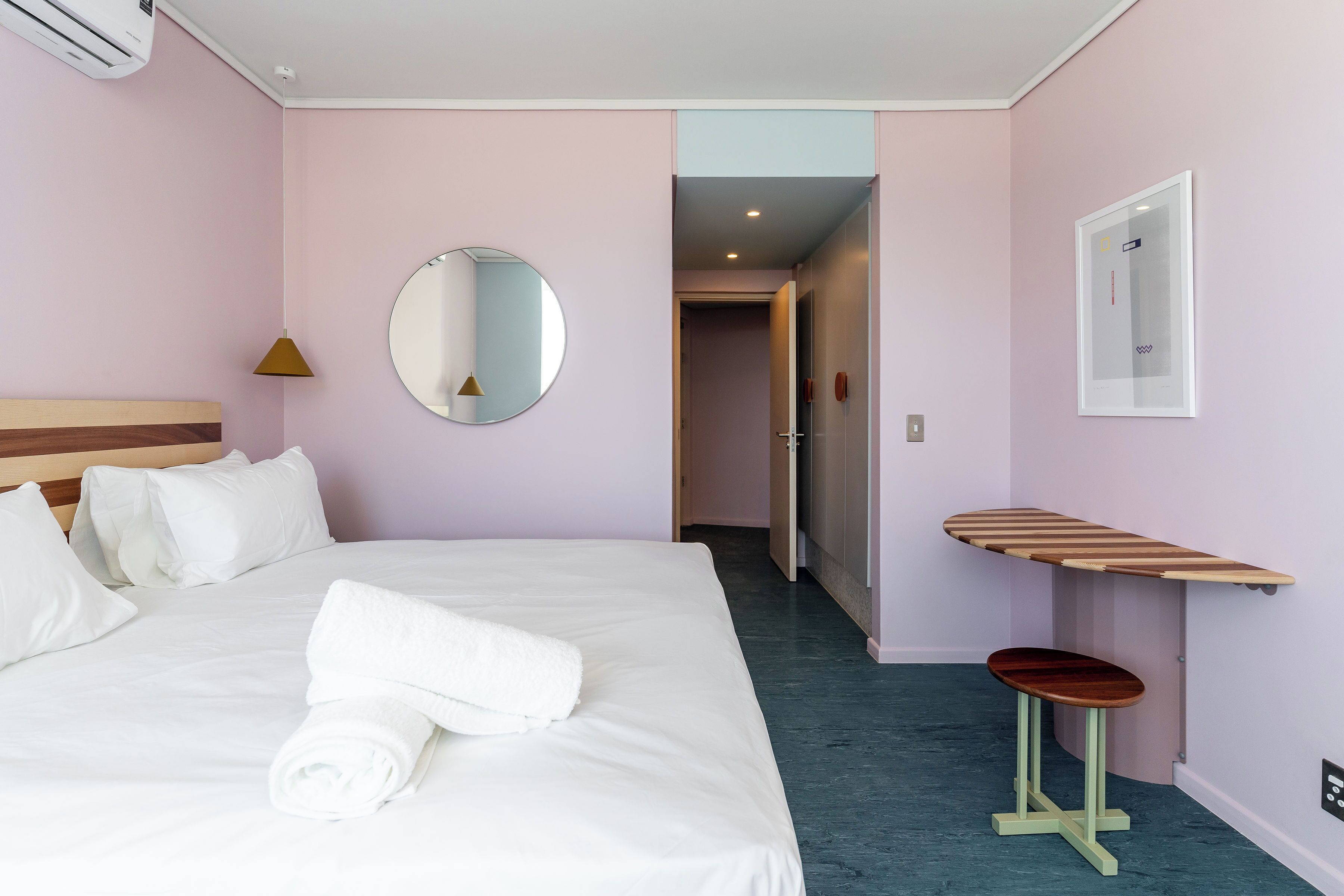 A hotel room with a bed, a bedside table, a mirror, and a door leading to another room.