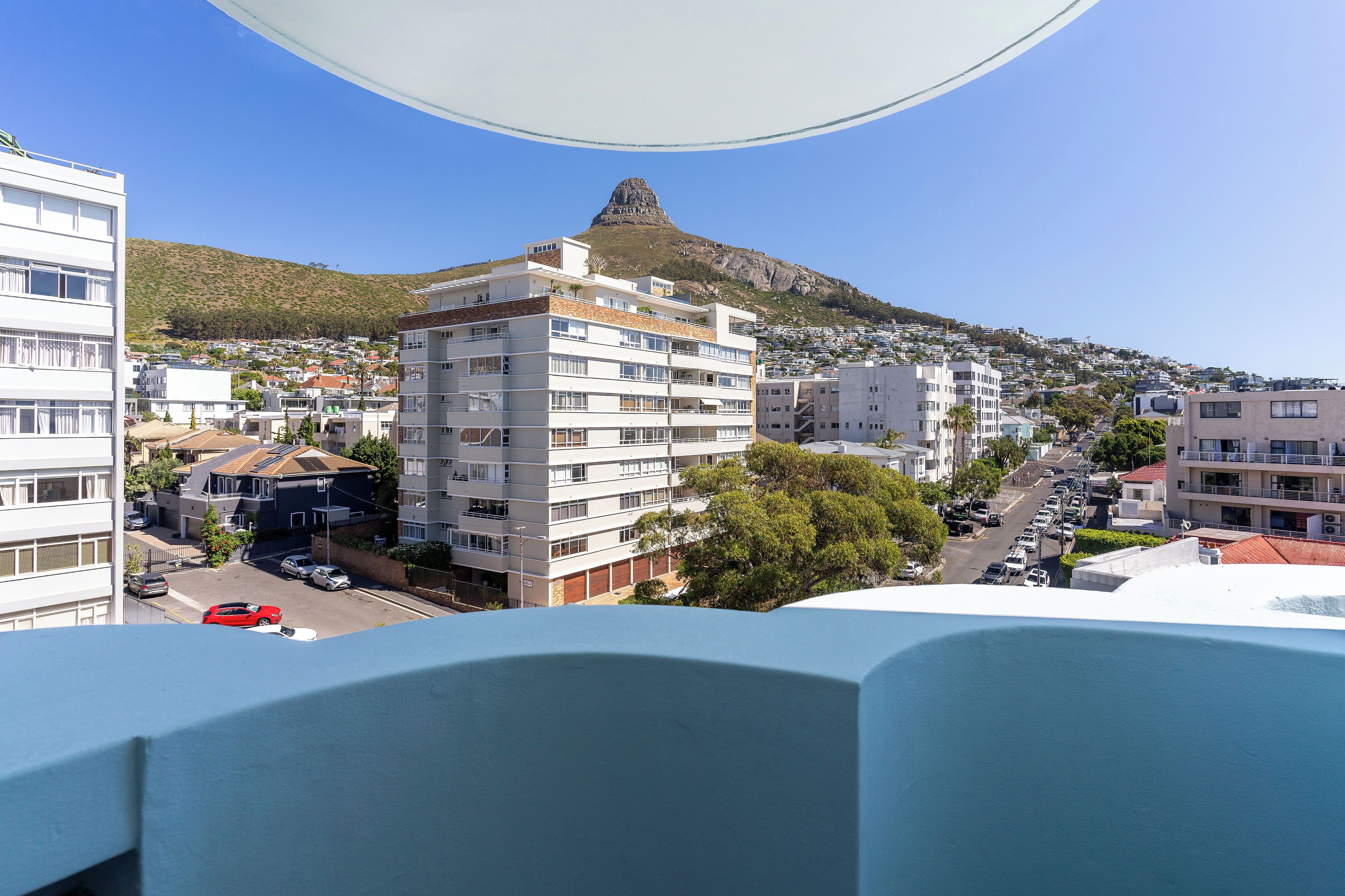 A residential area with multi-story buildings, a prominent mountain in the background, and a clear sky.