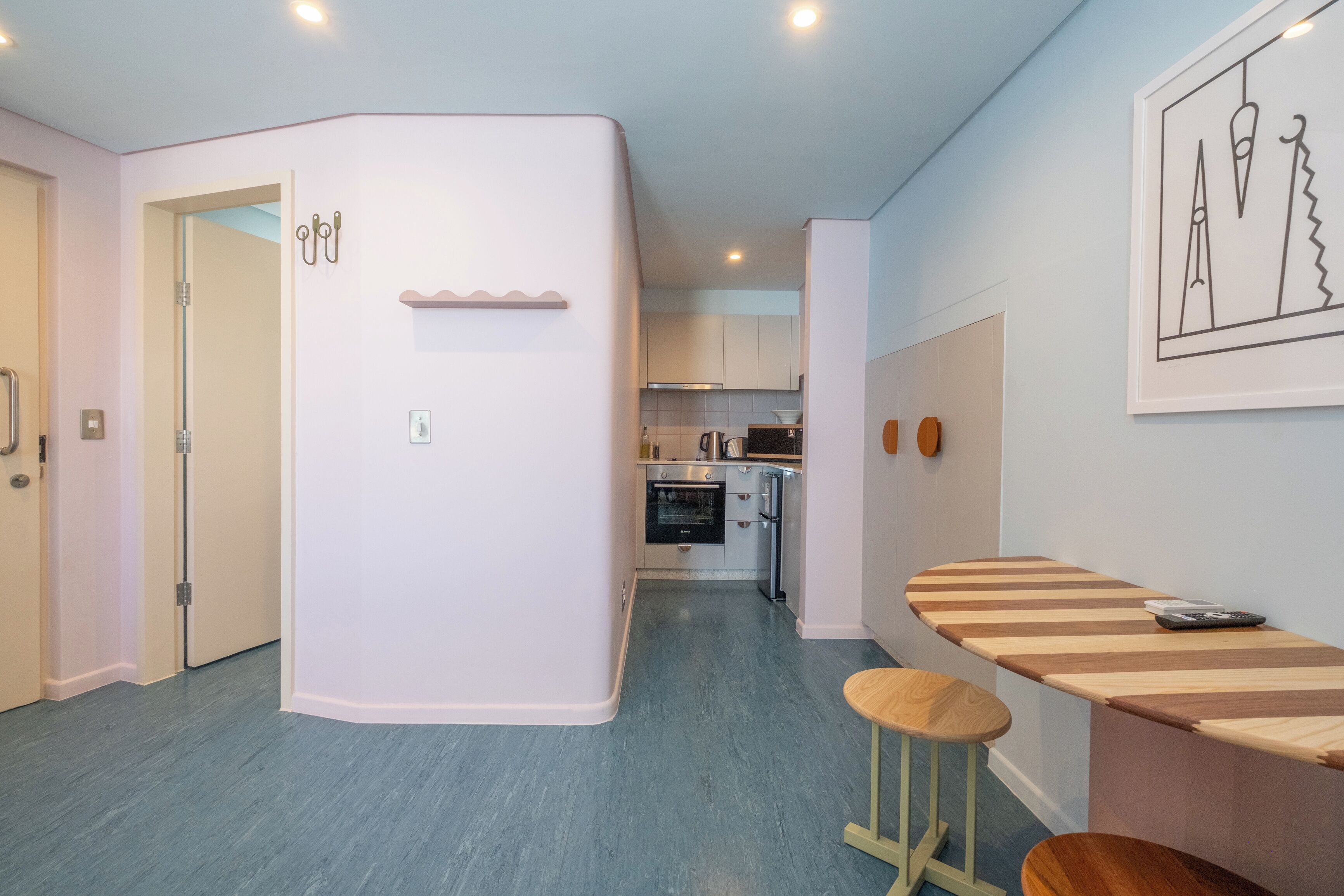 A compact kitchen with modern appliances, a dining area with a striped table, and a hallway leading to a door.