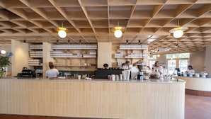 A modern restaurant with a central counter, wooden ceiling, and natural light from windows.
