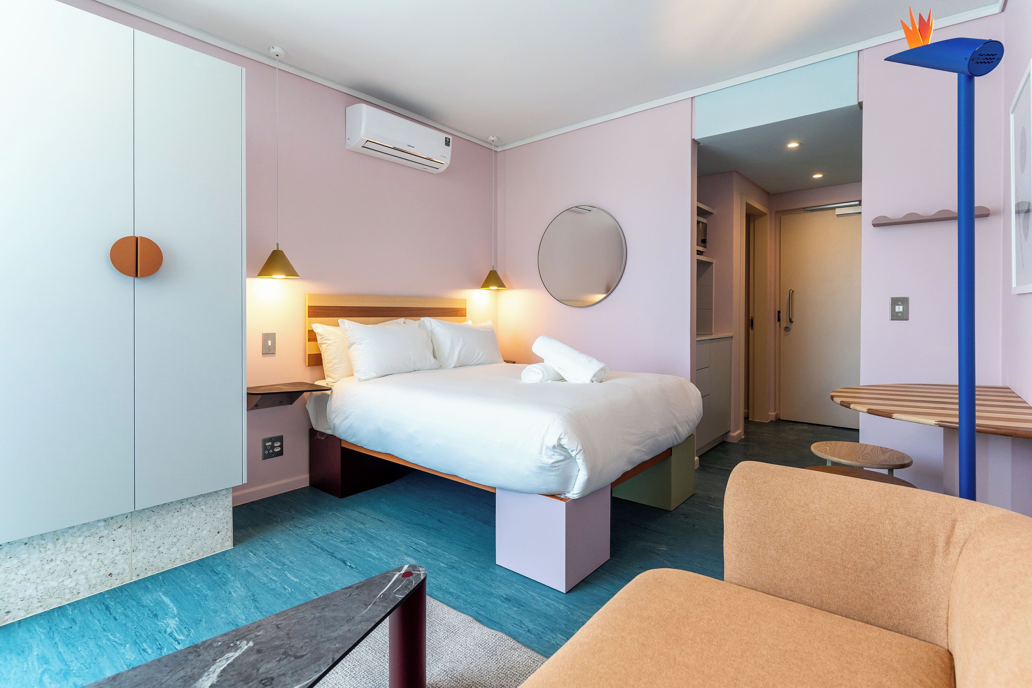 A modern hotel room with a bed, bedside table, and a round mirror on the wall.