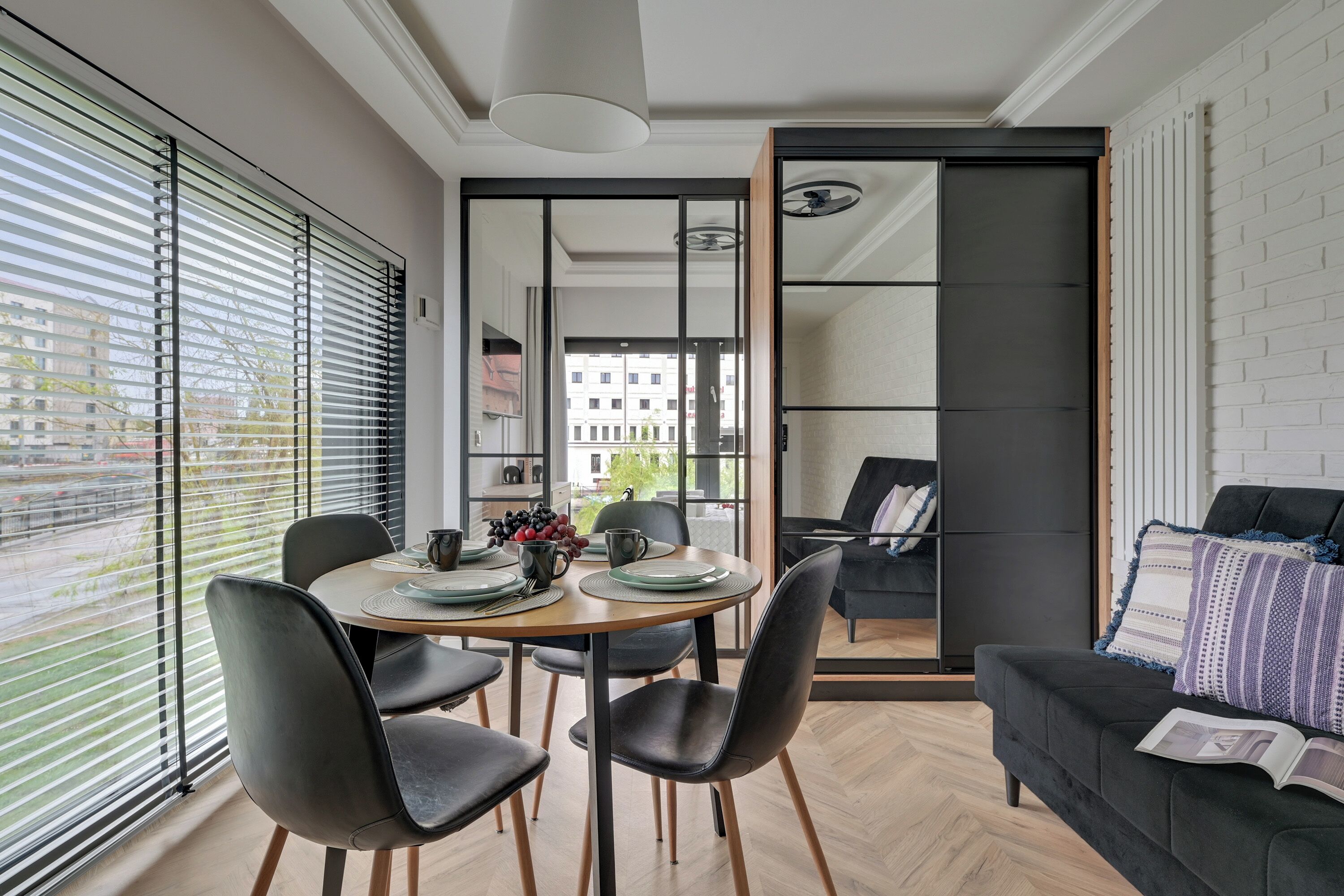 A modern dining area with a round table, black chairs, and a view through a glass door to an outdoor balcony.