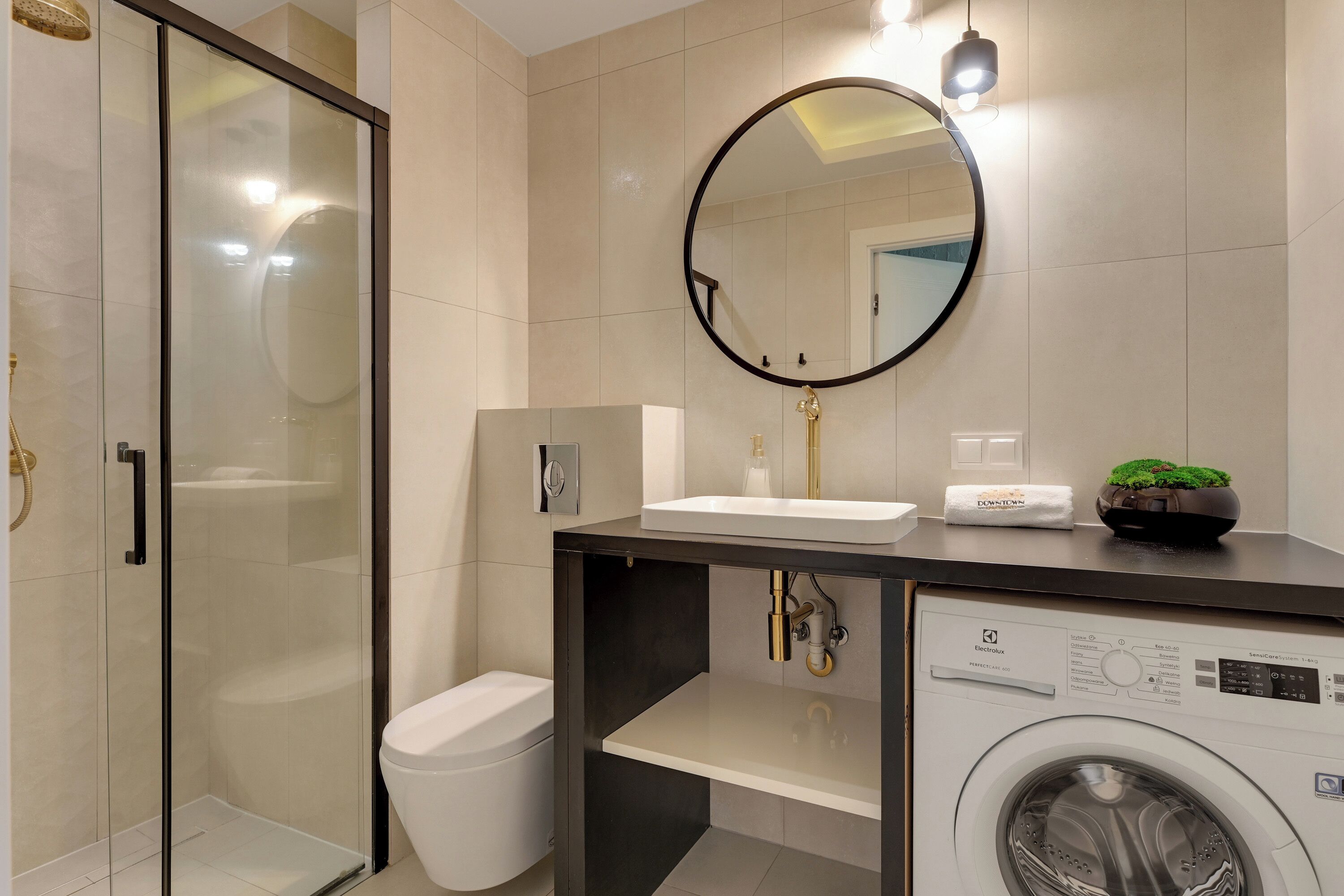 A modern bathroom with a glass shower enclosure, a sink with a mirror above, a toilet, and a washing machine.