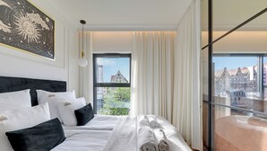 A hotel room with a large bed, a view of buildings, and a balcony.