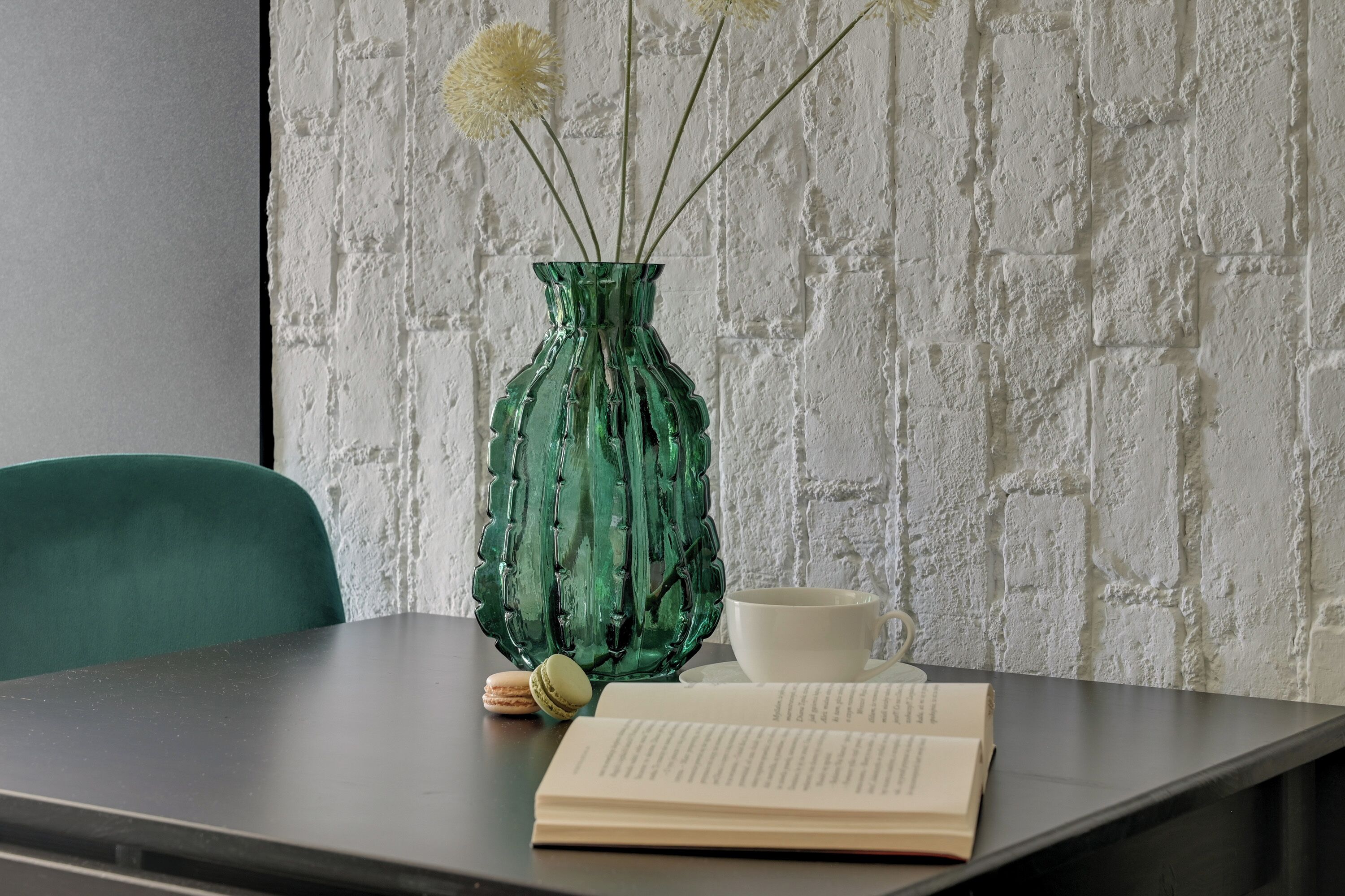 Una mesa con un jarrón verde, una taza blanca y un libro abierto.