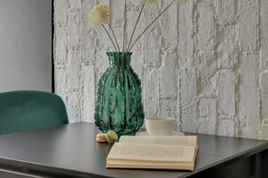 Una mesa con un jarrón verde, una taza blanca y un libro abierto.