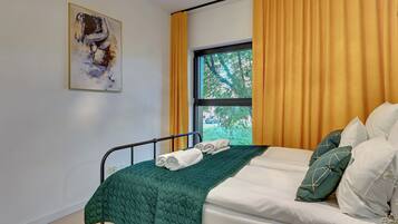 Una cama bien hecha con colcha verde, almohadas blancas y una ventana con cortinas amarillas.