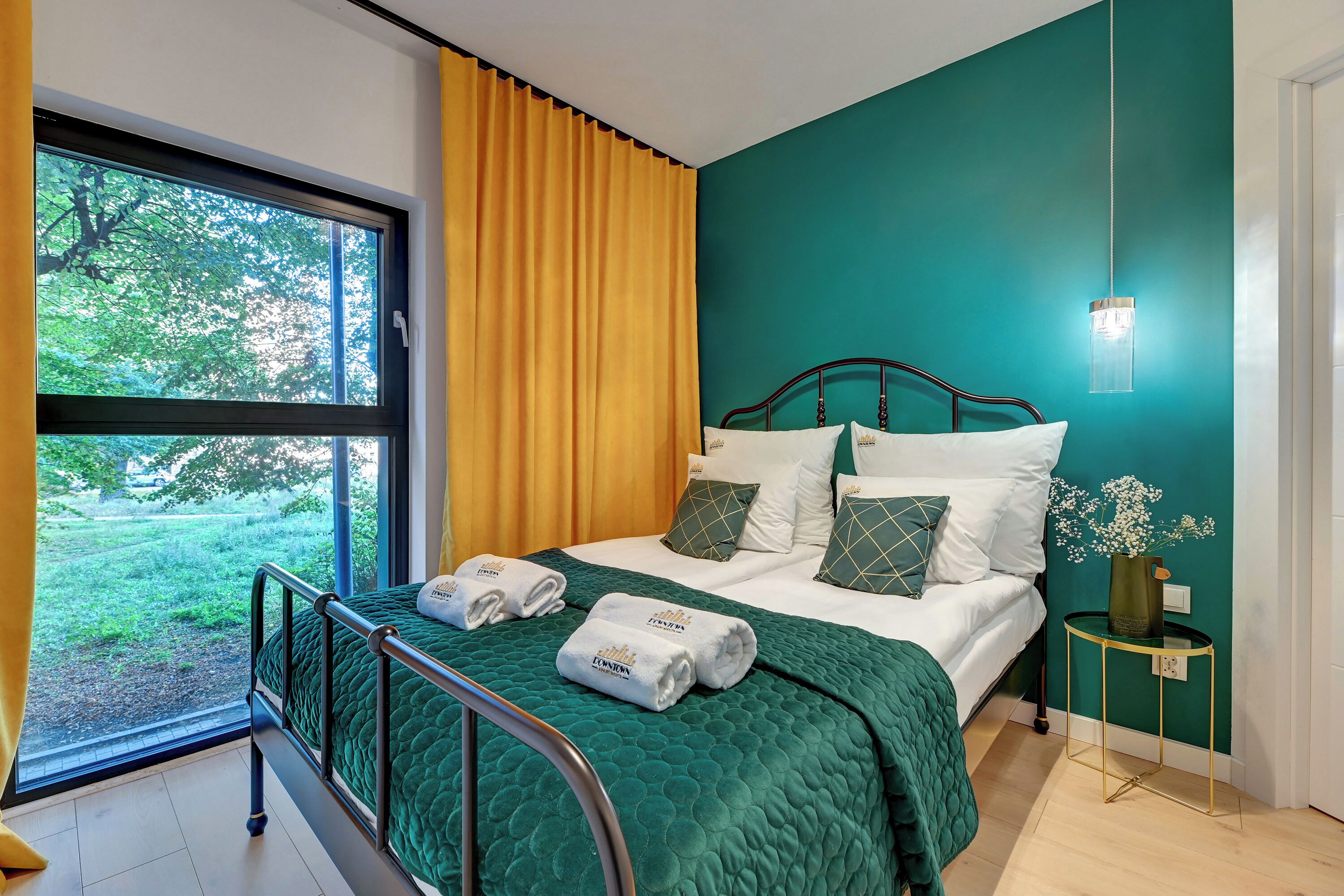 Ein ordentlich bezogenes Bett mit einer grünen Decke, weißen Kissen und Blick auf Grünfläche draußen.