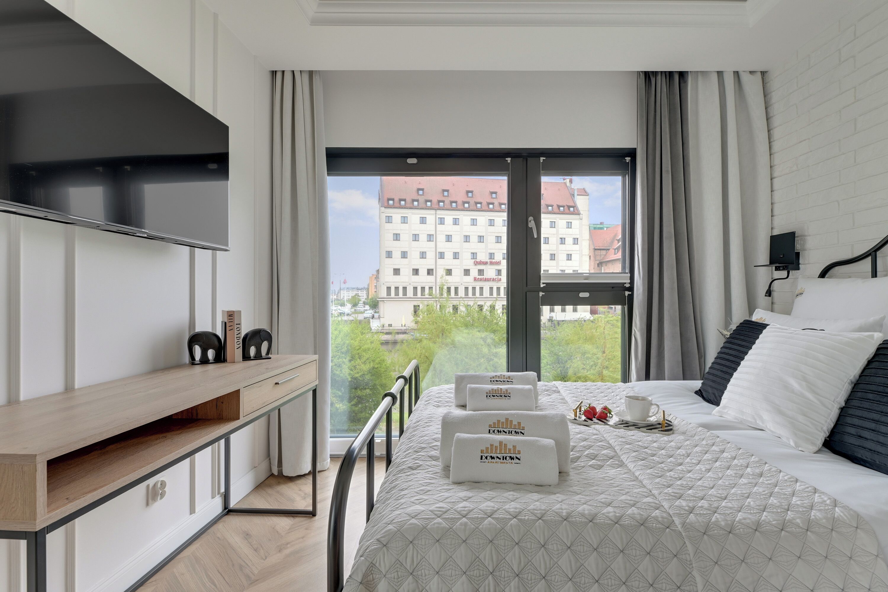 A modern hotel room with a bed, a desk, and a large window offering a city view.