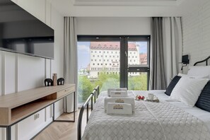 A modern hotel room with a bed, a desk, and a large window offering a city view. - Rezydencja Wintera by Downtown Apartments (Gdansk)