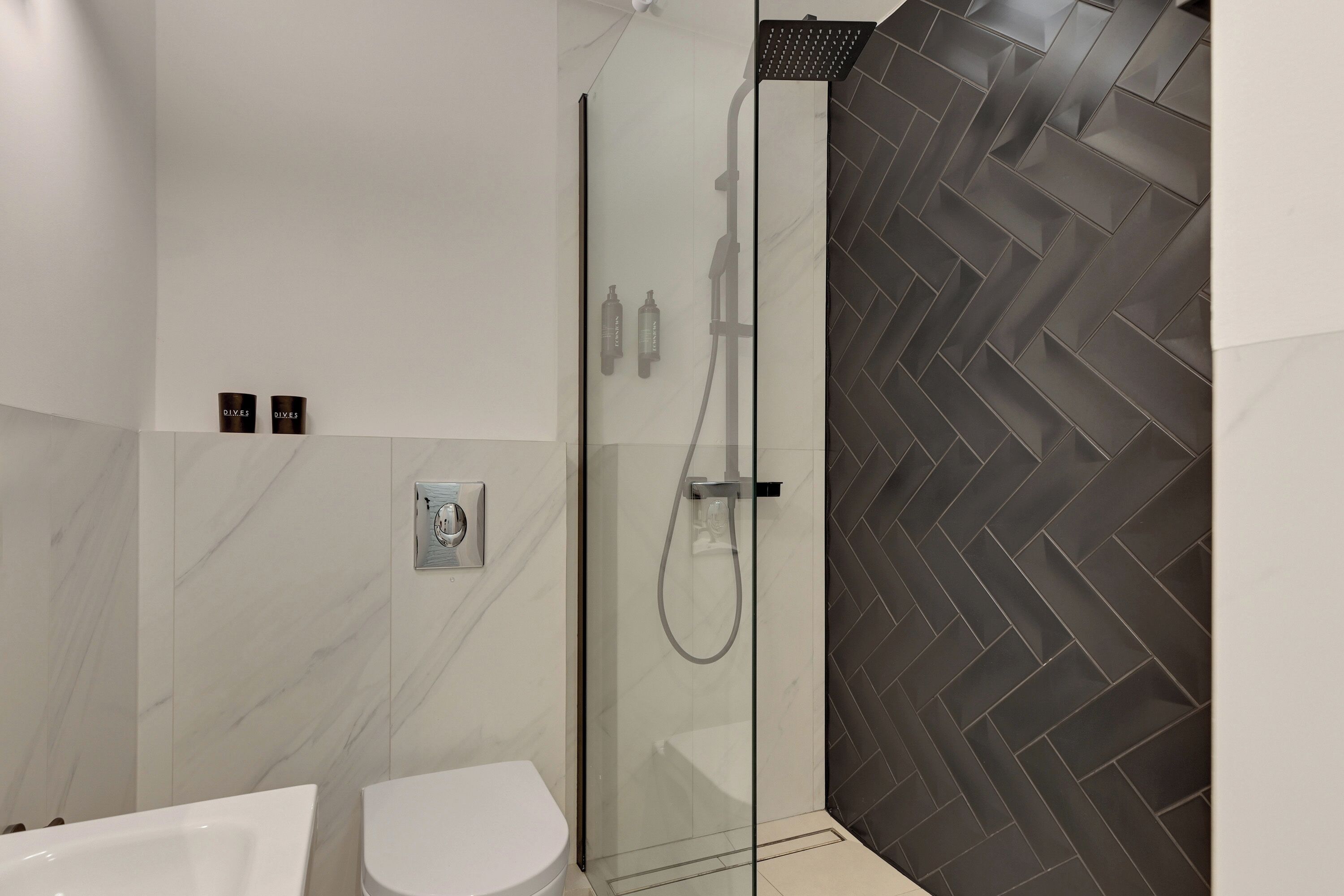A modern bathroom with a glass-enclosed shower, a white toilet, and a herringbone-patterned wall.