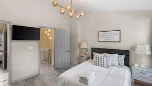 A bedroom with a bed, bedside tables, a lamp, a wall-mounted artwork, and a ceiling light fixture. - Golf Oasis Modern Townhome! (Charlotte)
