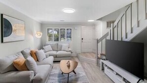 A modern living room with a sofa, coffee table, and a flat-screen TV. - Golf Oasis Modern Townhome! (Charlotte)