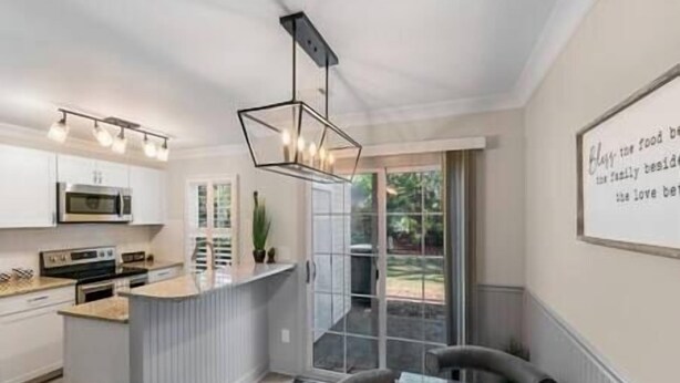 A modern kitchen with white cabinets, a built-in microwave, and a stainless steel oven. There is a large window providing a view of the outdoors. - Golf Oasis Modern Townhome! (Charlotte)