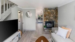 A modern living room with a stone fireplace, a flat-screen TV, and a staircase. - Golf Oasis Modern Townhome! (Charlotte)