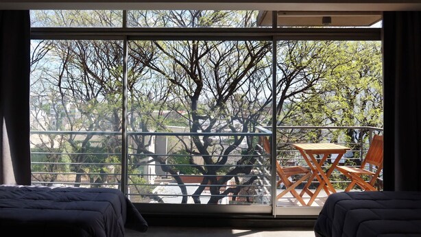 A room with a large window, a balcony with a table and chairs, and two beds. - Palermo Soho G4827 - Modern, Spacious and Luminous Apartments (Buenos Aires)