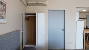 A compact living space with a grey couch, a wardrobe, a closed door, and a kitchen area with a refrigerator and a kettle. - Palermo Soho G4827 - Modern, Spacious and Luminous Apartments (Buenos Aires)