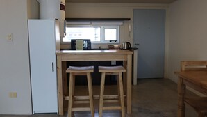 A compact kitchen with a white refrigerator, a microwave, and a kettle on the counter. There are two wooden stools and a wooden table. - Palermo Soho G4827 - Modern, Spacious and Luminous Apartments (Buenos Aires)
