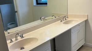 A bathroom with two sinks, a window, and a mirror.