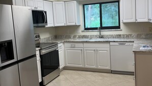 A modern kitchen with white cabinets, stainless steel appliances, and a window providing natural light.