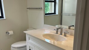 A modern bathroom with a white vanity, two sinks, a toilet, and a window.
