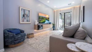 A modern living room with a sofa, a blue armchair, a TV, and a dining area with a table and chairs. - 5BR Stay Near Everything Orlando Offers (10382PG) (Orlando)