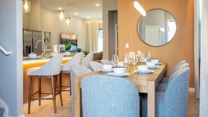 A modern dining area with a wooden table set for six, surrounded by blue upholstered chairs. - 5BR Stay Near Everything Orlando Offers (10382PG) (Orlando)