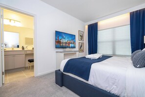Una habitación de hotel moderna con una cama grande, televisión, escritorio con silla y baño visible a través de una puerta abierta.