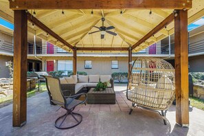 Un espacio de estar al aire libre cubierto con ventilador de techo, mobiliario de mimbre y una jaula de pájaros.