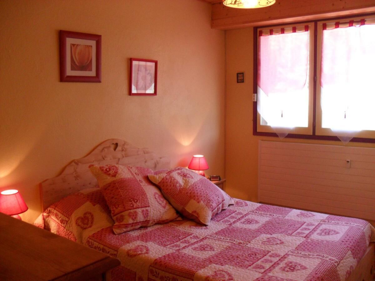 Een slaapkamer met een bed, twee bedlampen, een raam met gordijnen en twee ingelijste foto's aan de muur.