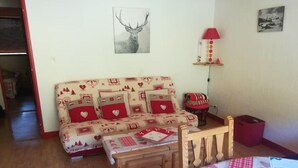 Ein gemütliches Zimmer mit einer gemusterten Couch, einem Holzstuhl, einem kleinen Tisch und einer Lampe.