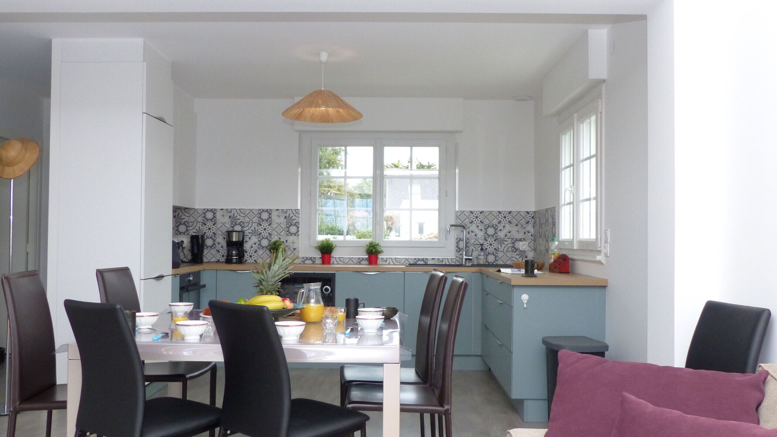 A modern kitchen with a dining area, featuring a central island, a coffee maker, and a window with a view.