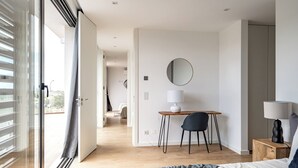 A modern bedroom with a bed, bedside tables, a desk, and a chair. There is a large window with blinds, a mirror on the wall, and a view of the outside. - Hazel Yellow Villa, Sintra, Lisbon (Sintra)