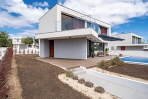Et moderne hus i to etager med fladt tag, balkon med glasgelændere, swimmingpool og en velholdt have.