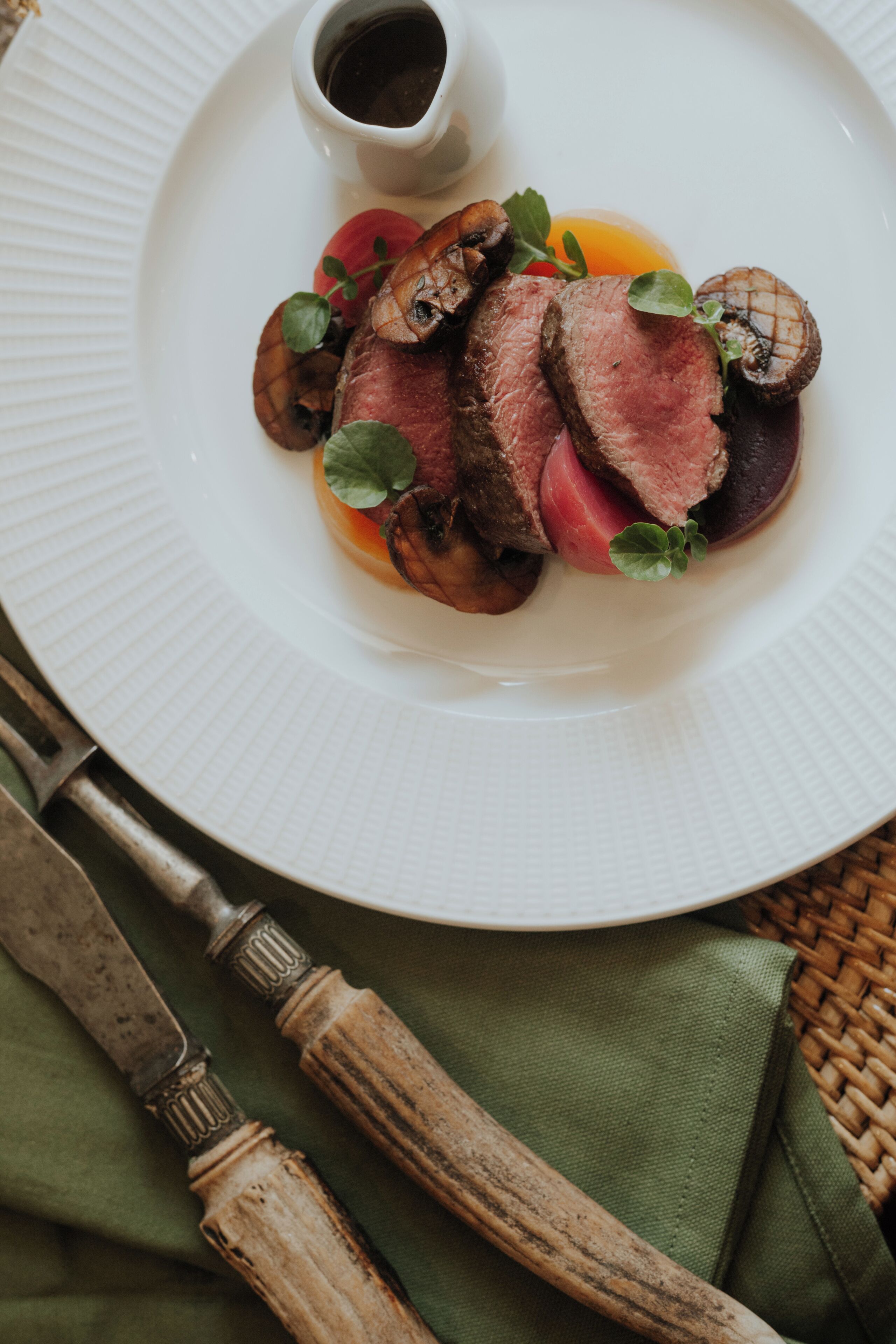 A plate of sliced meat with mushrooms and a small bowl of sauce.