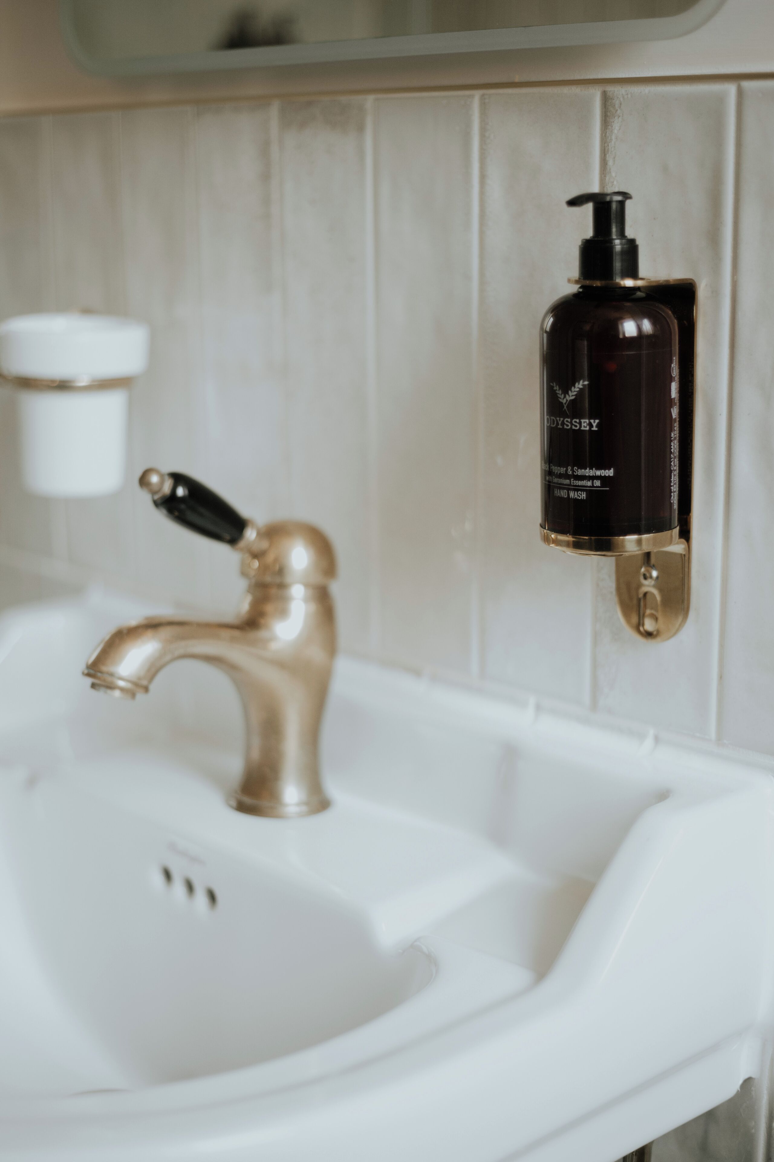 Un lavabo de salle de bain avec un robinet doré et un distributeur de savon noir fixé au mur.
