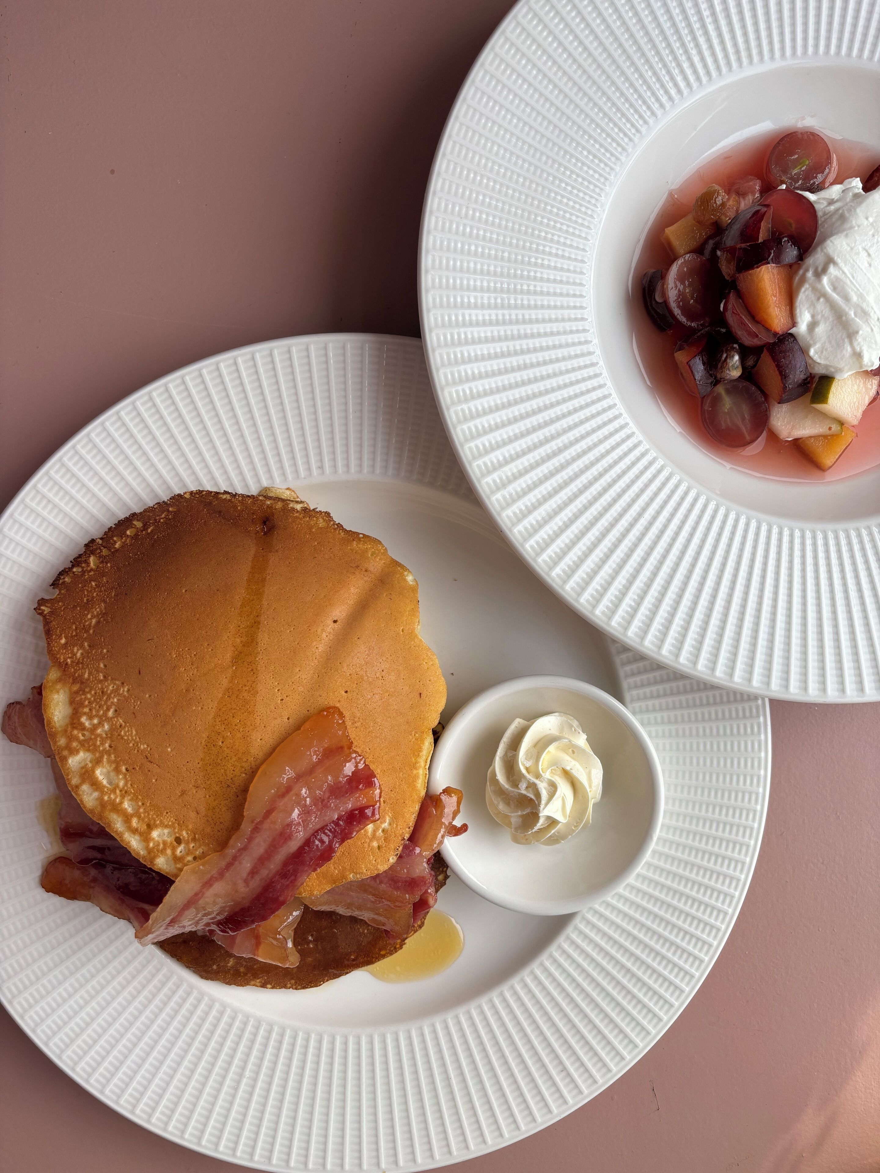 Mesa de café da manhã com panquecas, bacon e uma tigela de frutas.