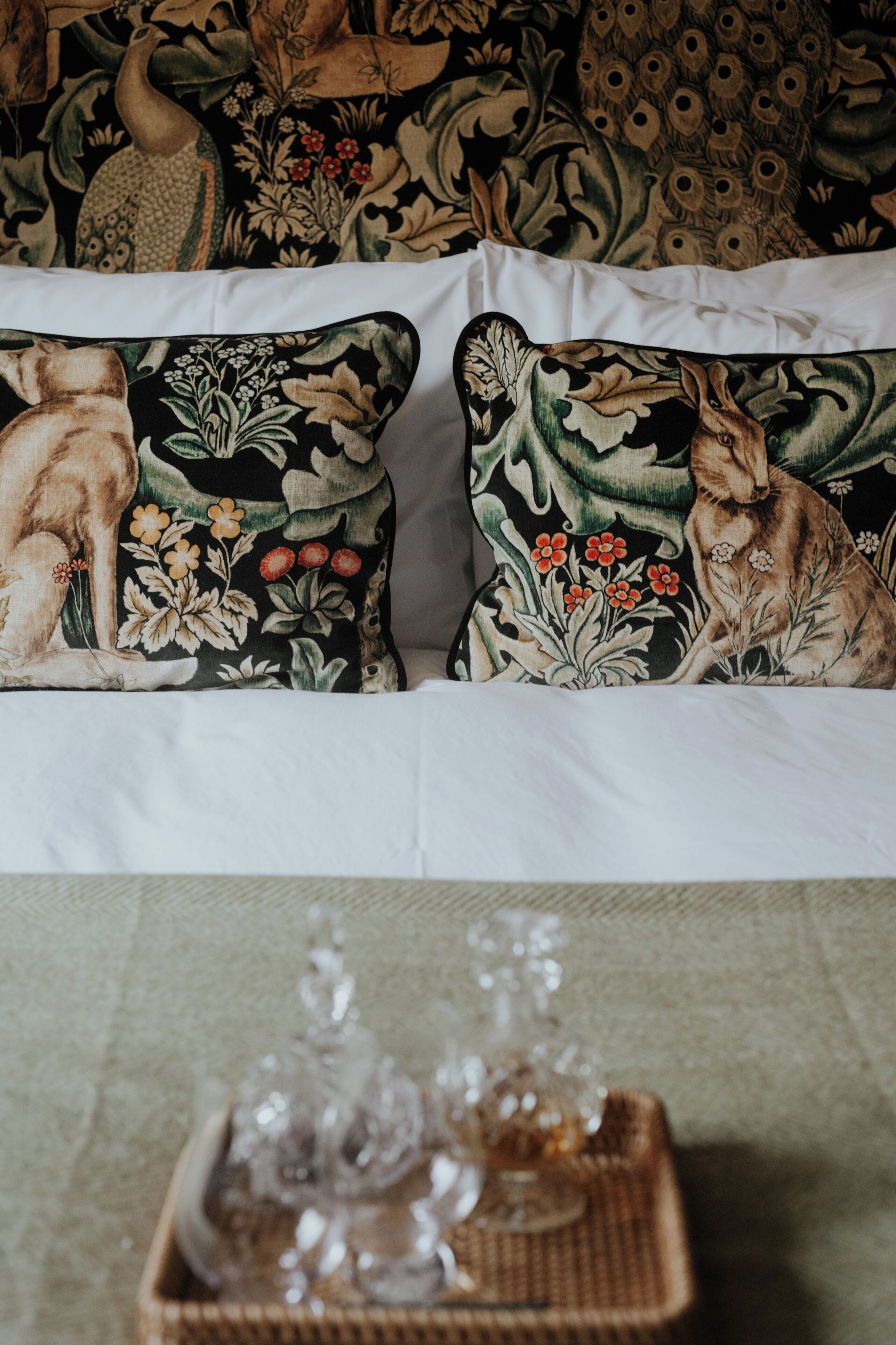 A bed with floral-patterned pillows and a wicker tray with glassware.